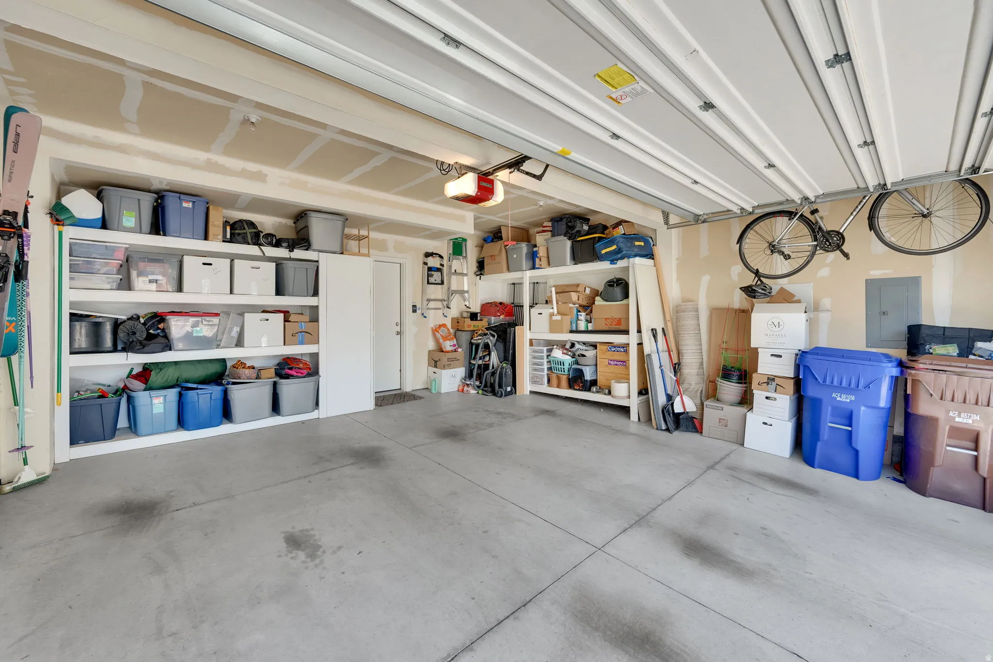 Spacious garage with exposed beam ceiling, concrete flooring, built-in shelving, a side door entry, and an automatic garage door opener