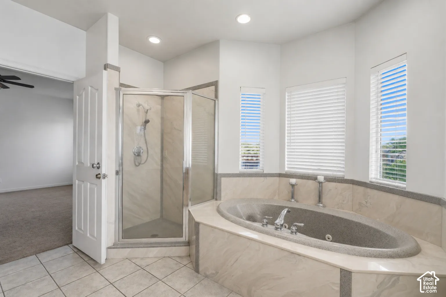 Soaking tub with integrated jets, glass-enclosed shower, tile flooring, and multiple windows with horizontal blinds