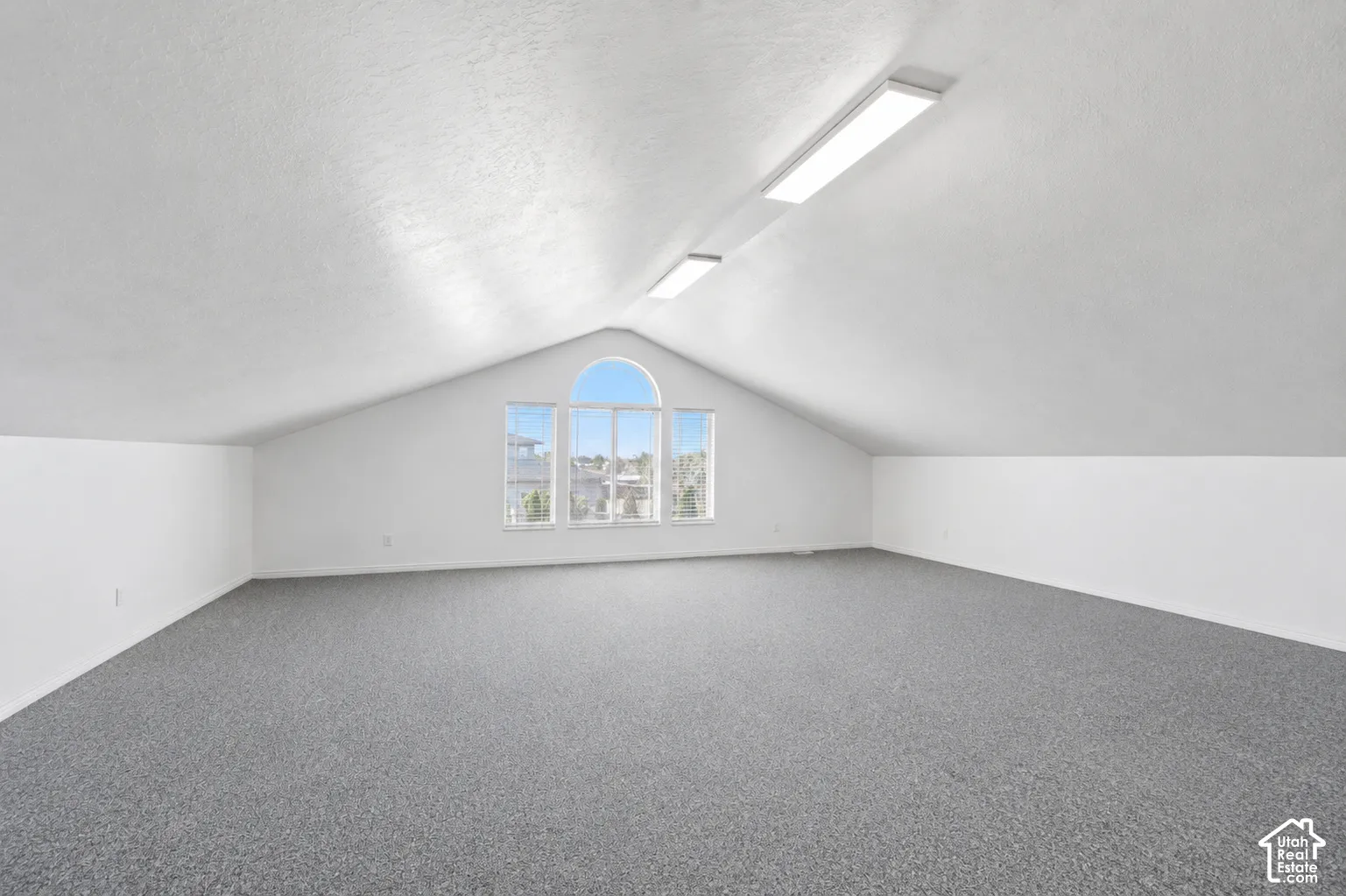 Open loft space with sloped ceilings, white walls, and gray carpeting