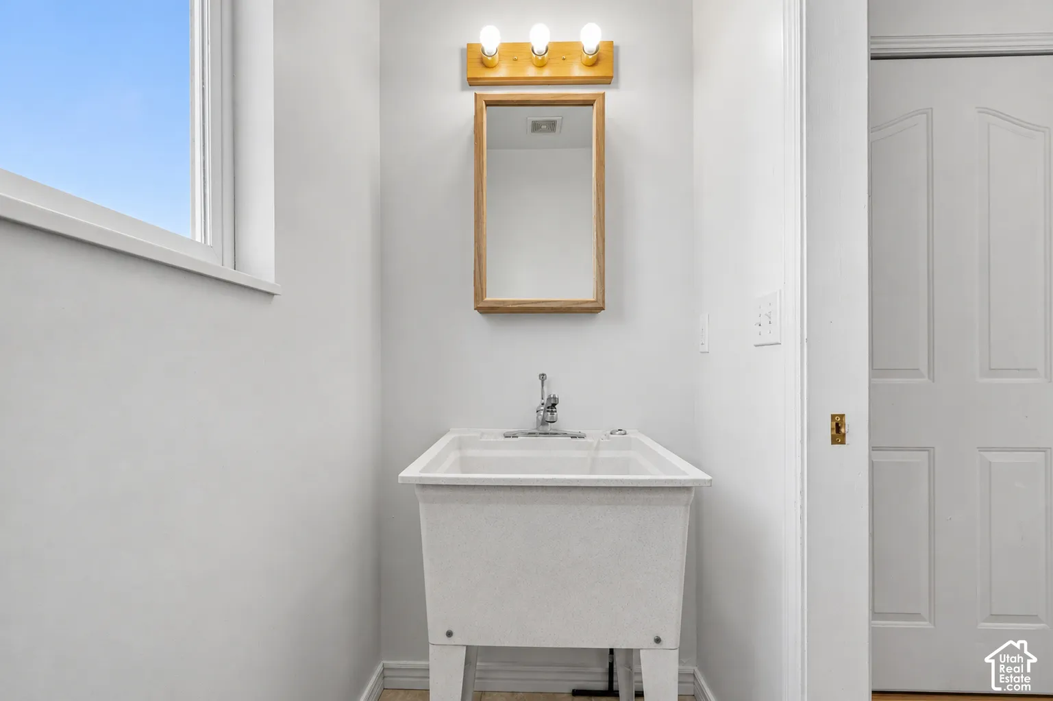 Utility sink with chrome faucet, framed mirror, triple vanity light, and a single window