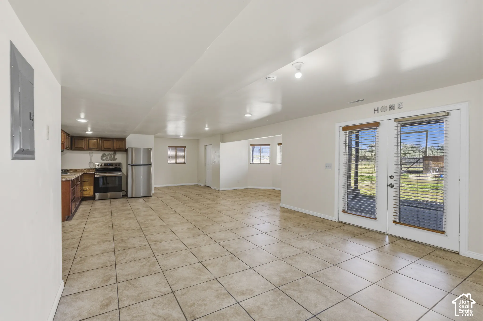 Open-concept living space with tiled flooring, recessed lighting, and a full kitchen with wood cabinetry and stainless steel appliances