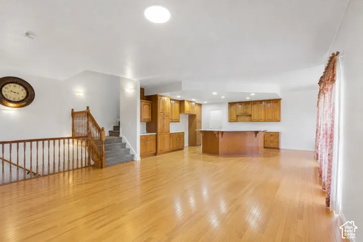 Hardwood flooring, wood-finish cabinetry, a central kitchen island, staircase with wood banister, and recessed lighting