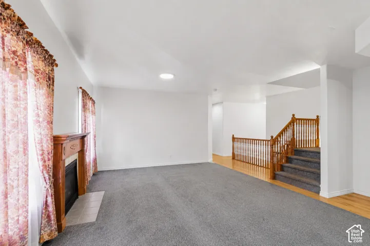 Spacious interior featuring a wood-finish staircase, carpeted flooring, and a fireplace with a wood mantel