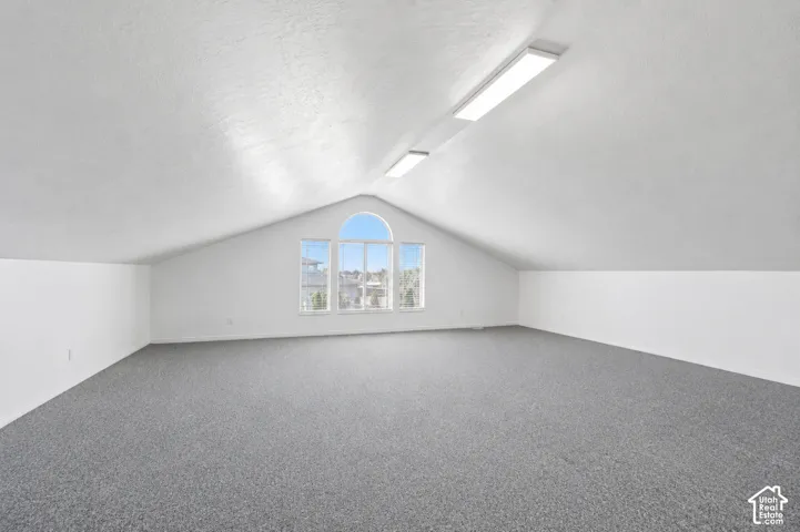 Open loft space with sloped ceilings, white walls, and gray carpeting