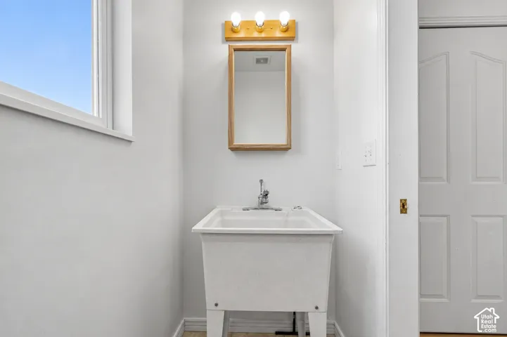 Utility sink with chrome faucet, framed mirror, triple vanity light, and a single window