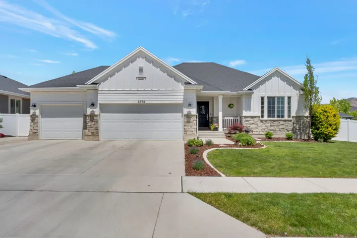 Contemporary ranch-style residence featuring a two-car garage, stone and board-and-batten siding, a covered porch entry, a concrete driveway, and a manicured lawn with established landscaping