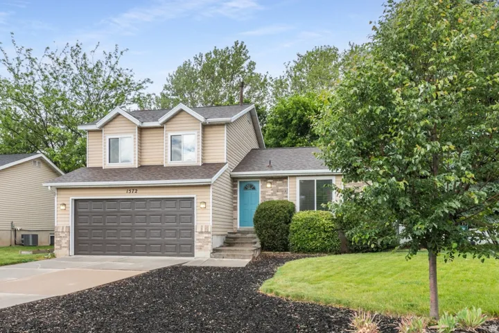 Two-story residence featuring light beige siding, a two-car garage, and a vibrant turquoise front door
