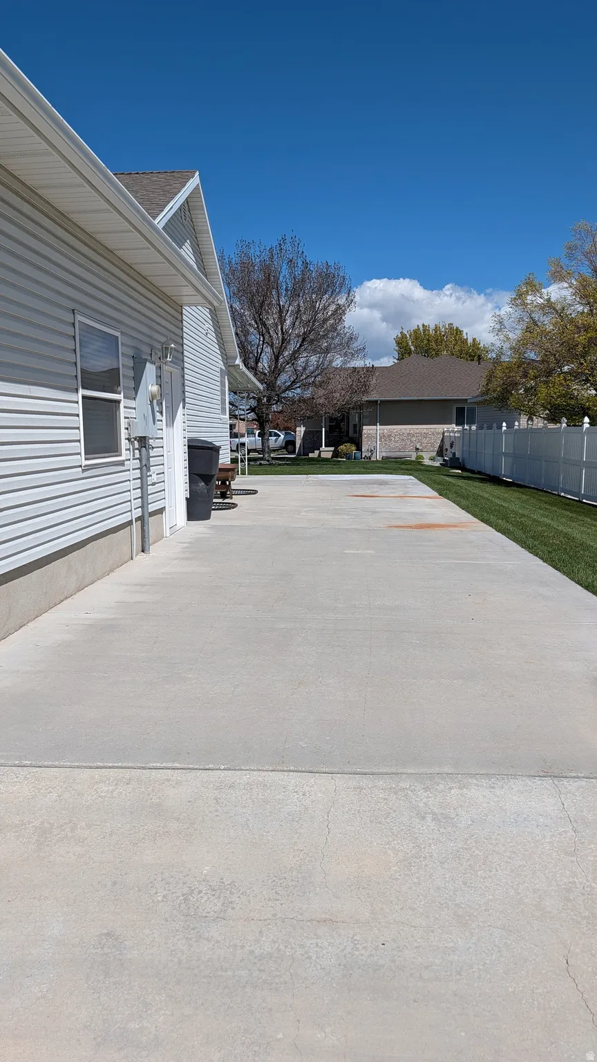 Extended concrete driveway and parking area bordered by a manicured lawn and white privacy fencing