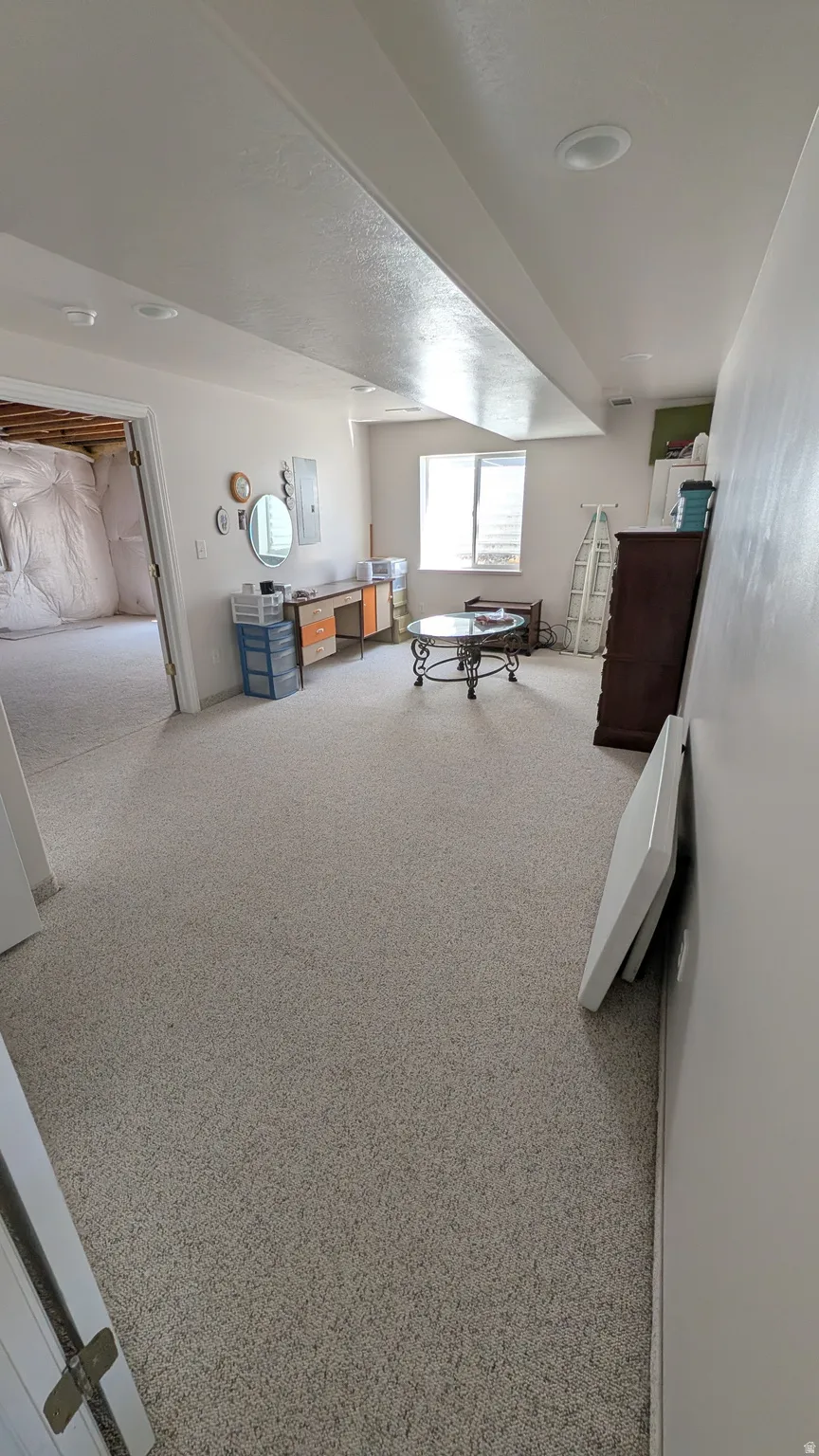 Spacious room featuring light-toned carpeting, recessed ceiling lighting, a window providing natural light, and a doorway opening to an unfinished area