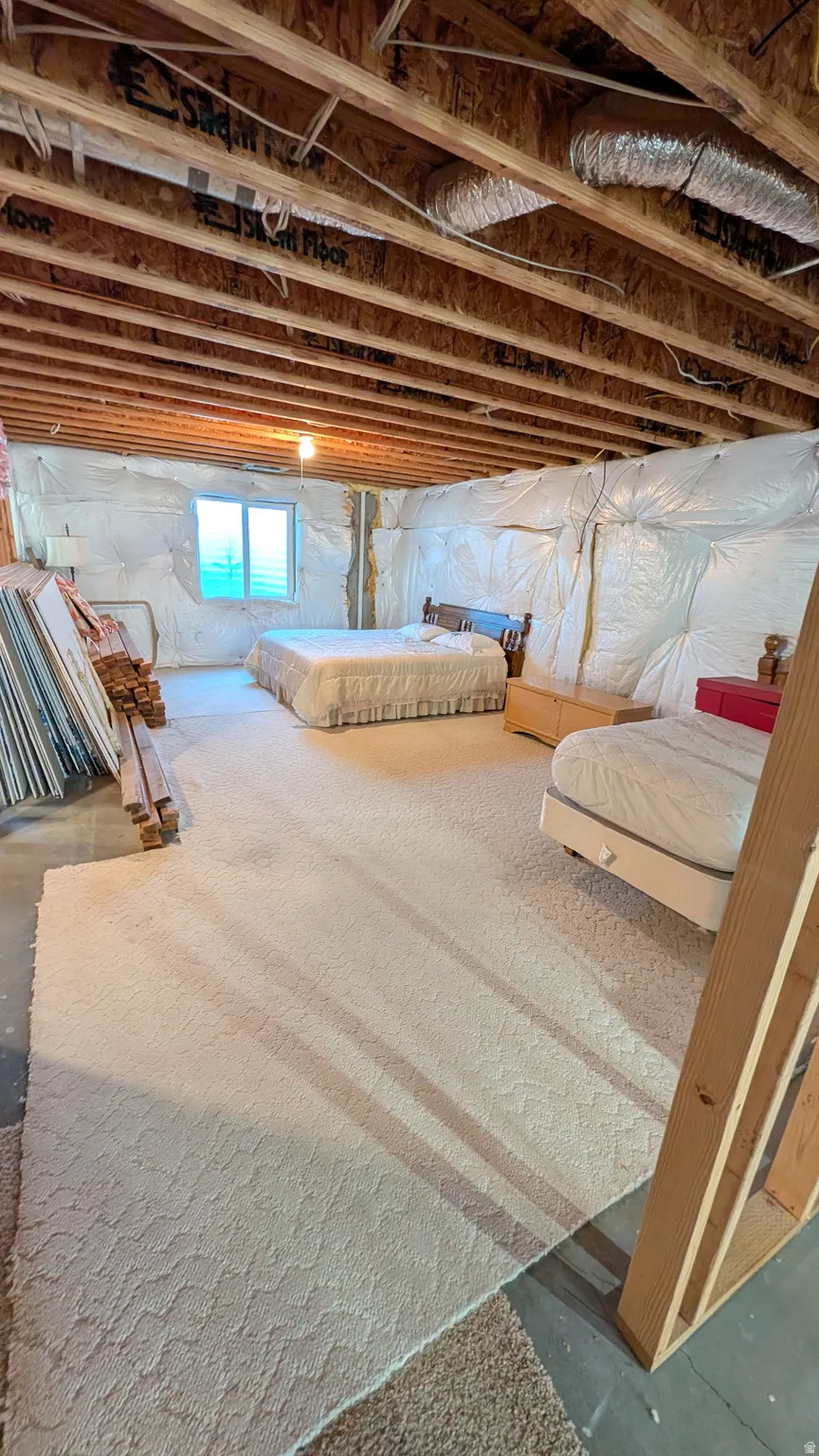 Lower-level space featuring exposed wood joists, a window opening, and insulation-wrapped walls