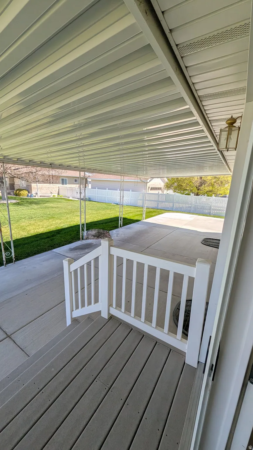 Covered patio featuring a solid roof, an outdoor wall sconce, and a white picket gate