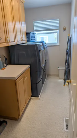 Utility room featuring light wood cabinetry, a light-colored countertop, and light-toned carpet flooring