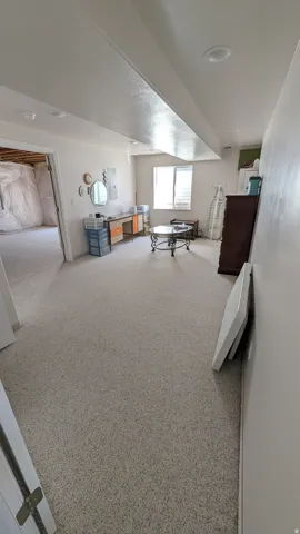 Spacious room featuring light-toned carpeting, recessed ceiling lighting, a window providing natural light, and a doorway opening to an unfinished area