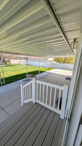 Covered patio featuring a solid roof, an outdoor wall sconce, and a white picket gate