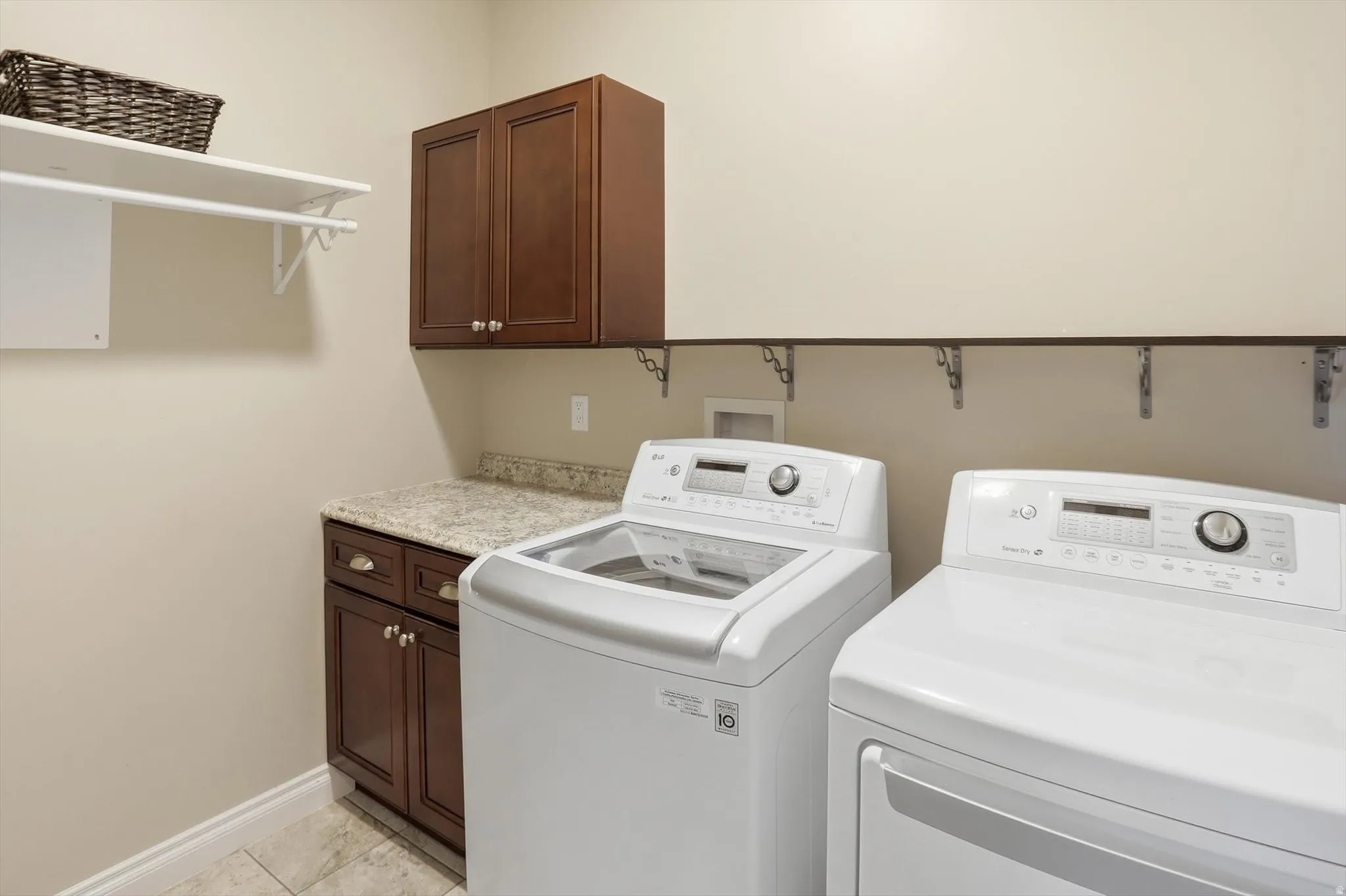 Dedicated laundry space featuring dark wood-finish cabinetry, a light-toned countertop, and tiled flooring