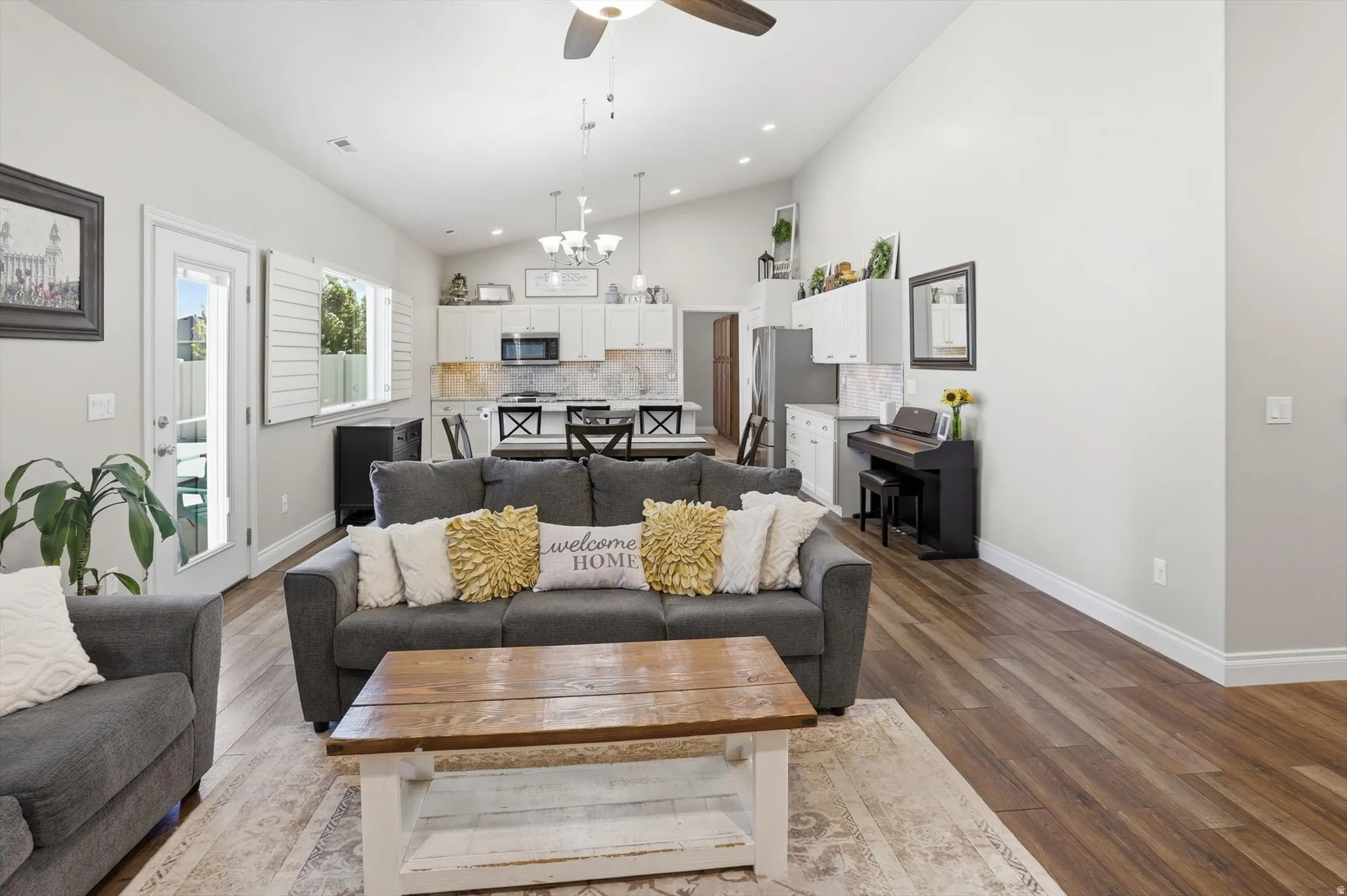 Spacious living area featuring vaulted ceilings, wood-finish flooring, and white plantation shutters