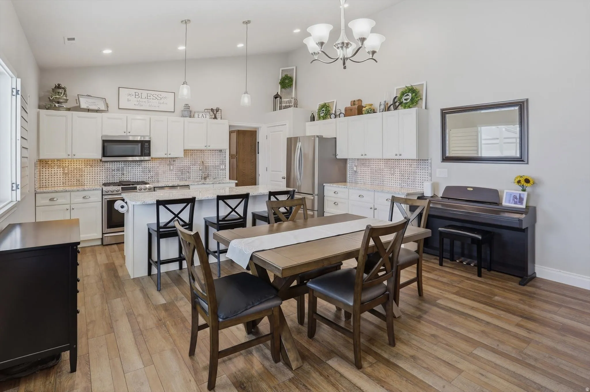 Open-concept kitchen and dining area featuring vaulted ceilings, wood-finish flooring, white cabinetry, a kitchen island with seating, and stainless steel appliances