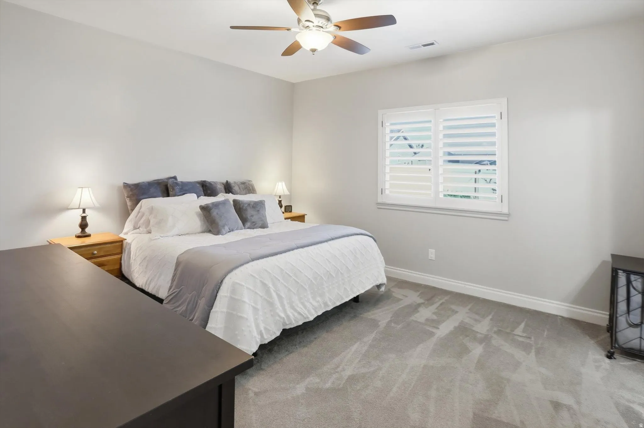 Carpeted room with a ceiling fan, window featuring white plantation shutters, and light gray wall paint