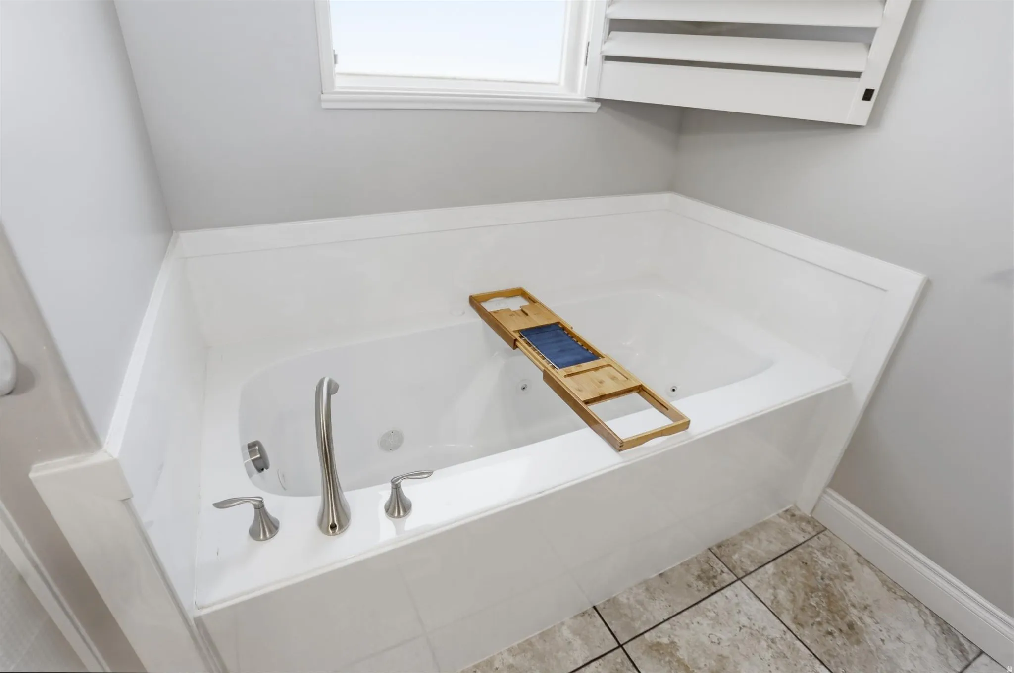 Built-in soaking tub with brushed nickel fixtures, white paneling surround, and tiled flooring