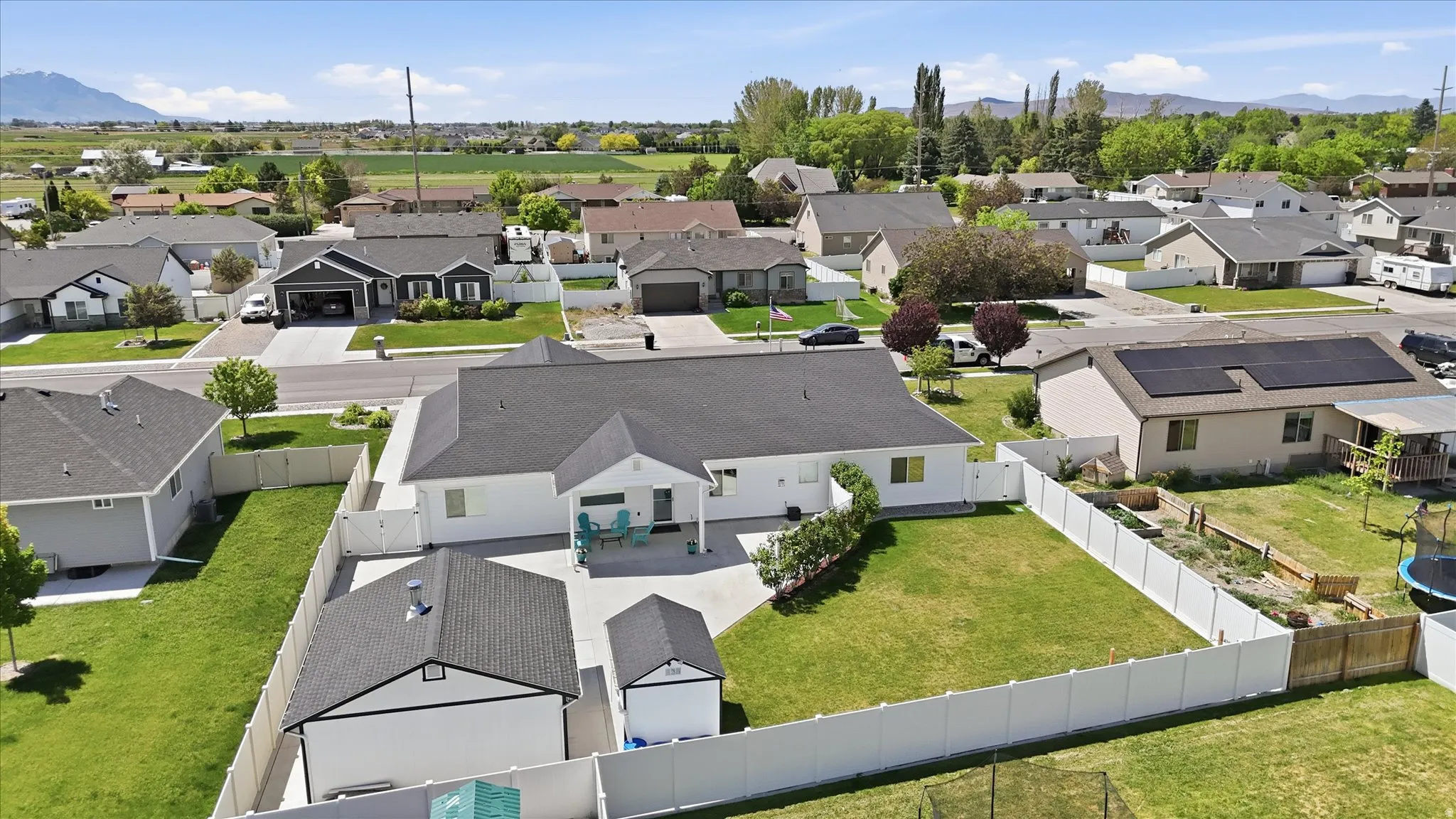 Expansive backyard featuring a manicured lawn, white vinyl fencing, a detached shed, a paved patio, and a covered porch