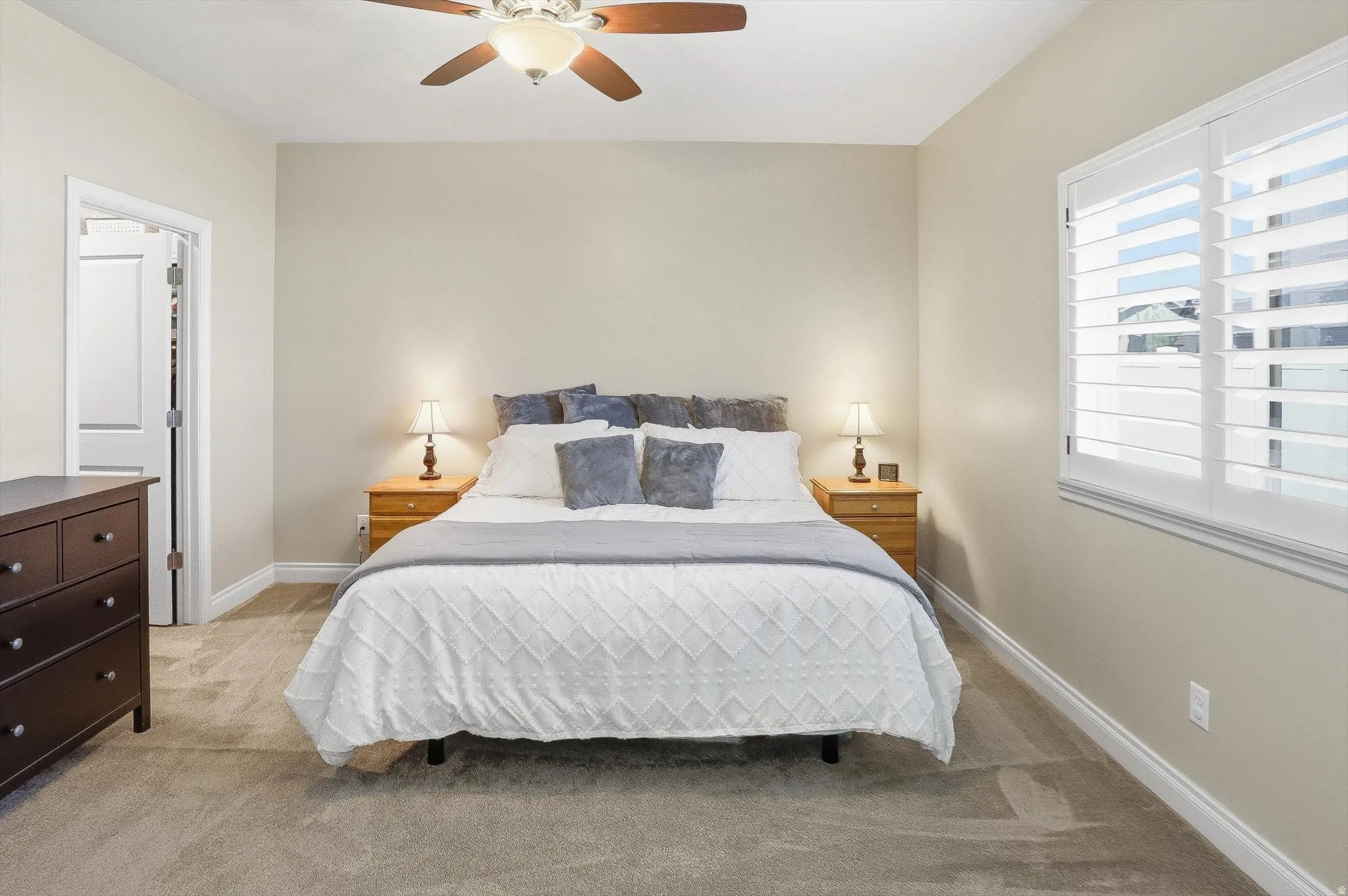 Bedroom featuring neutral-toned walls, plush carpeting, a ceiling fan with light fixture, and a window with white plantation shutters