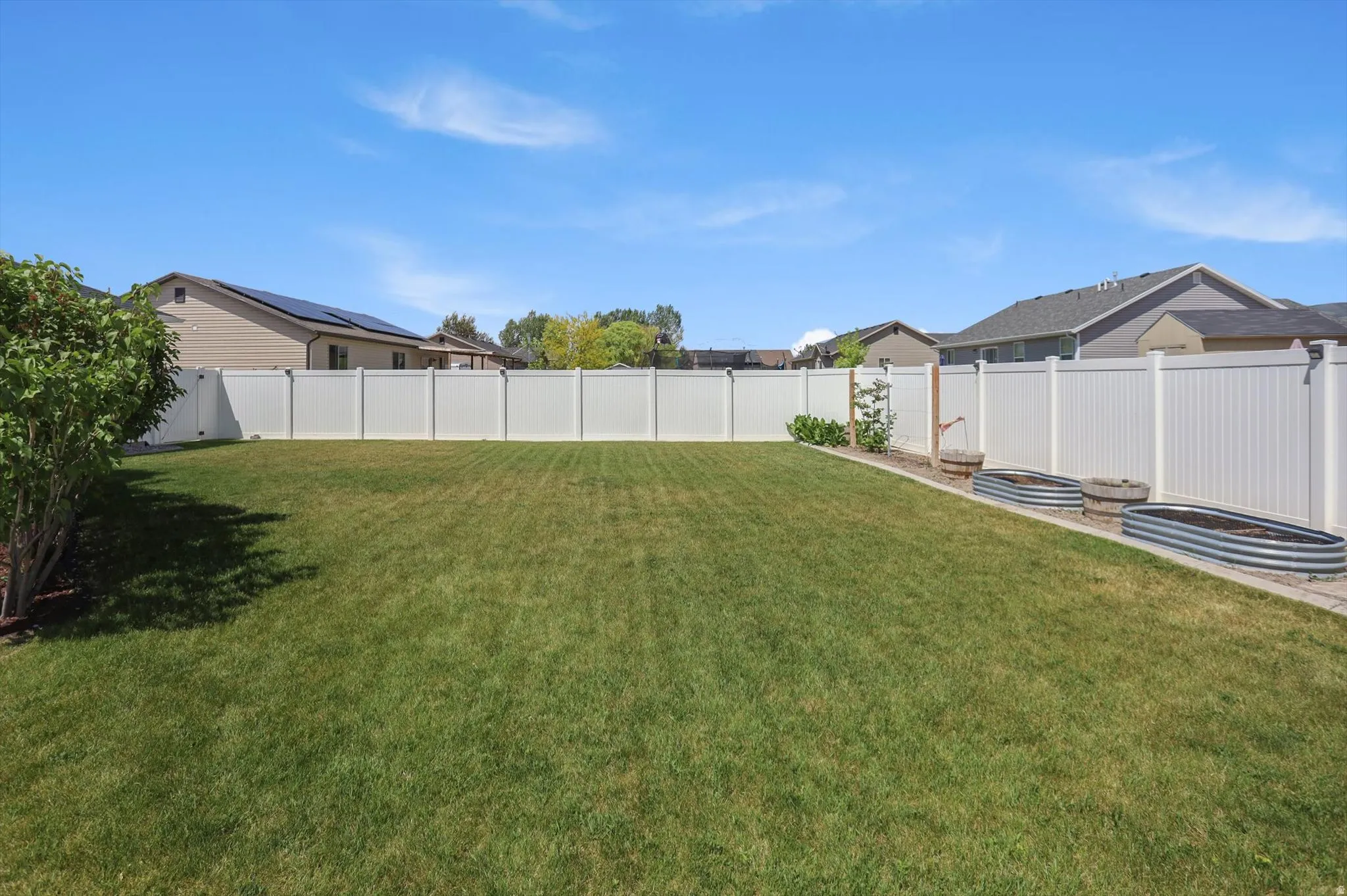 Expansive backyard featuring a large lawn, white privacy fencing, and a built-in garden bed with corrugated metal planters
