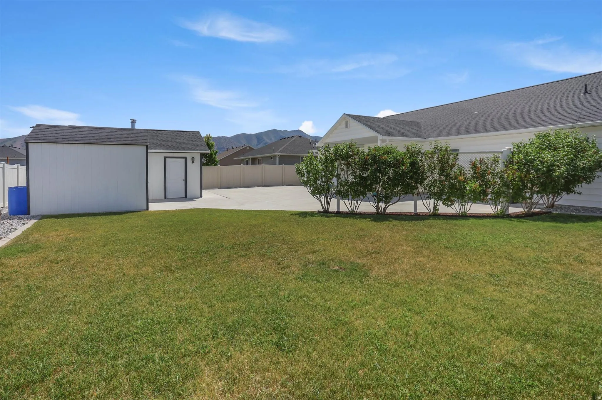 Expansive lawn with a separate storage shed, concrete driveway, and mature shrubbery bordering the main structure