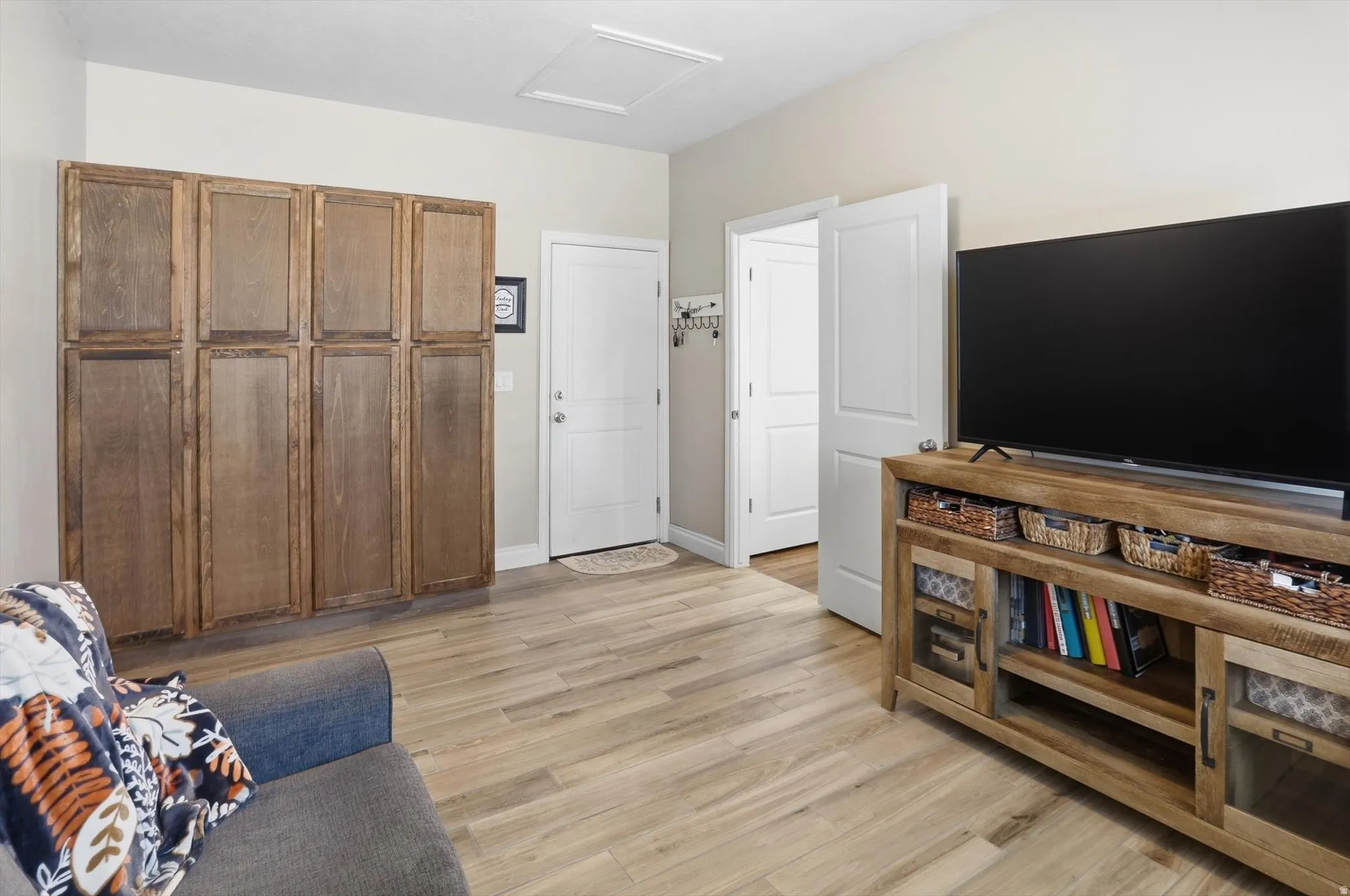 Spacious room featuring extensive built-in wood-finish cabinetry, light wood-finish flooring, two white panel doors, and a ceiling access panel