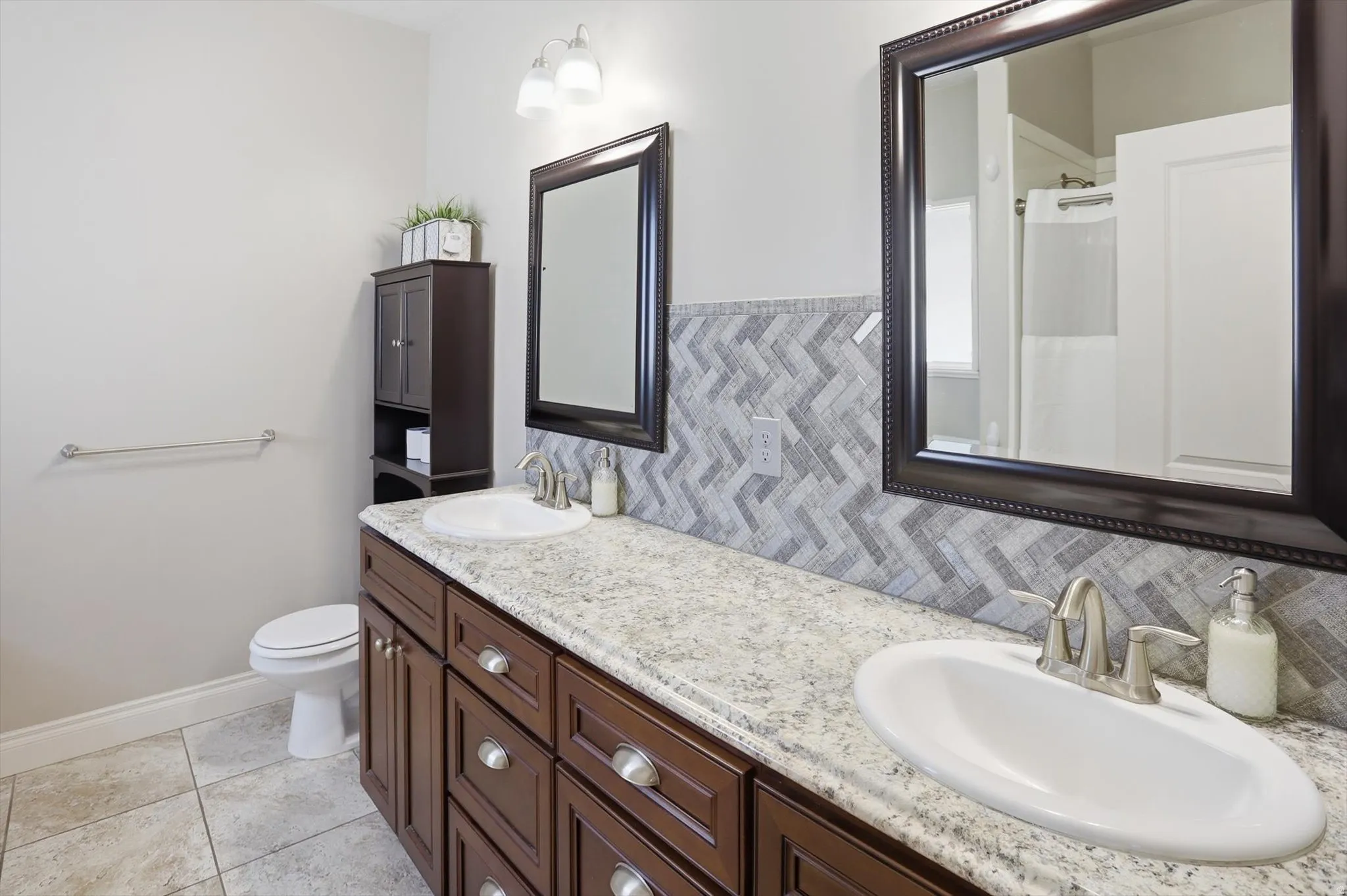 Bathroom featuring a double vanity with wood cabinetry, light-colored speckled countertops, and undermount sinks