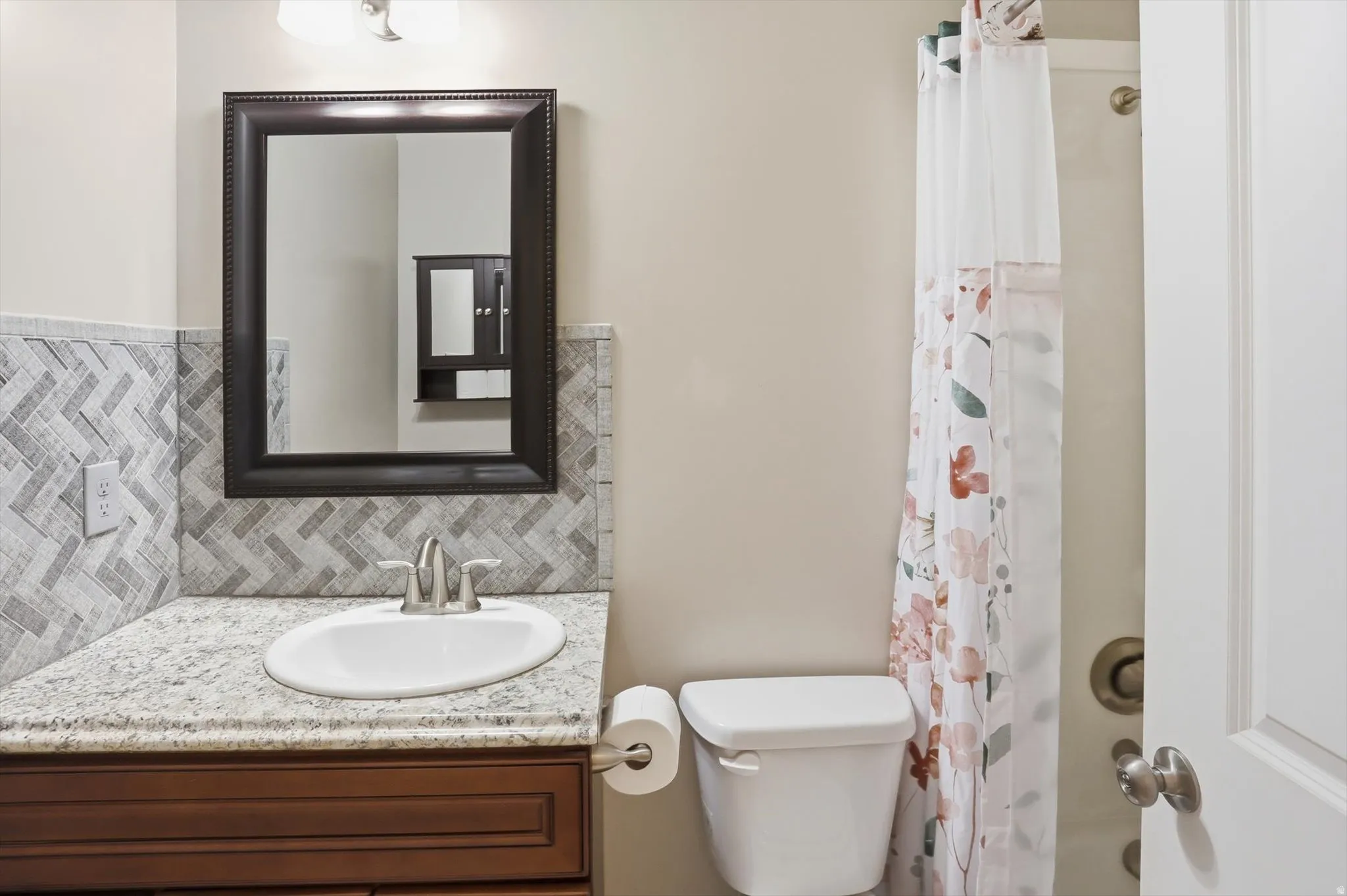 Bathroom featuring a vanity with granite-style countertop, herringbone tile backsplash, and a framed mirror
