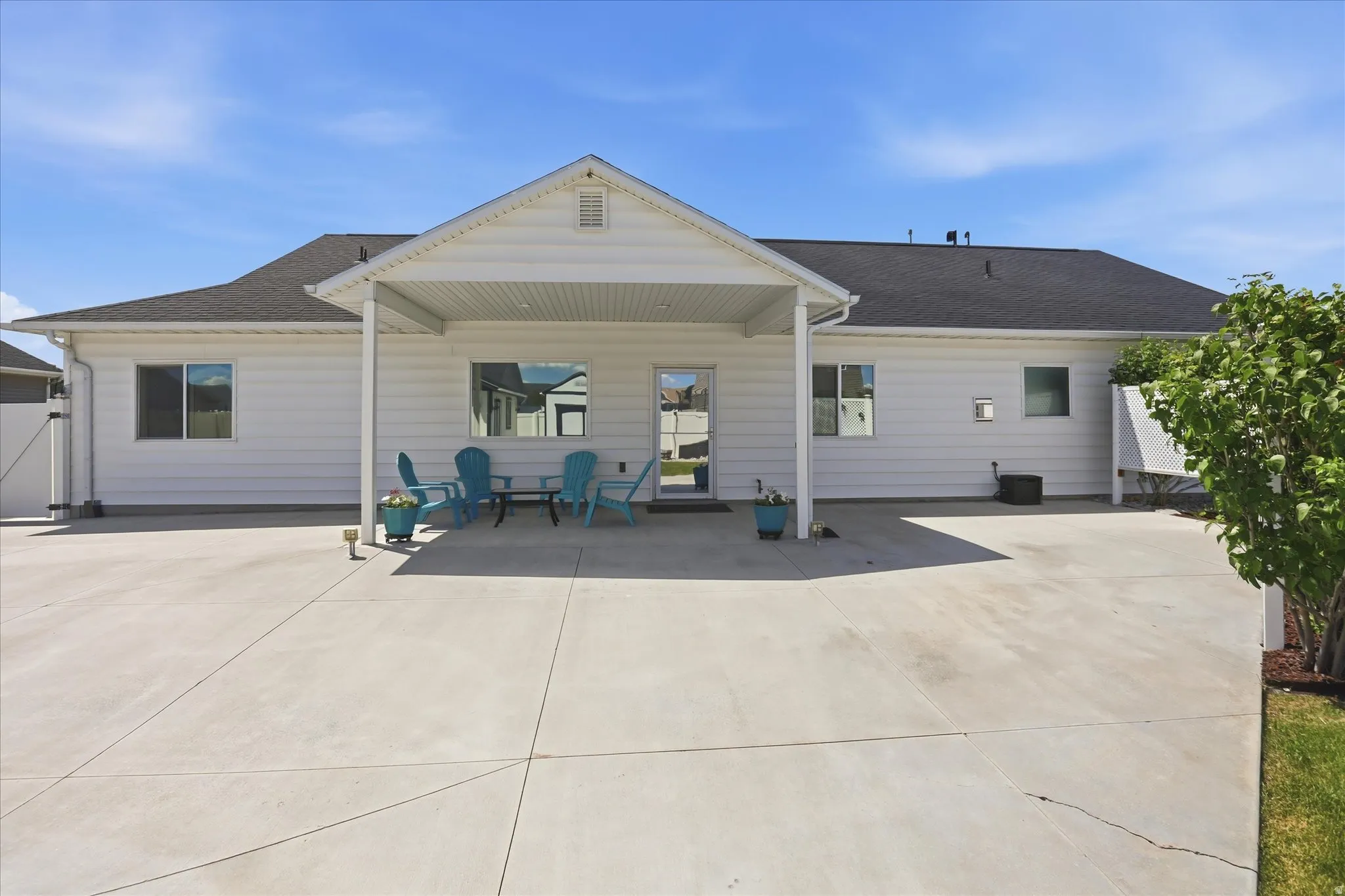 Spacious concrete patio with a covered outdoor area, white vinyl siding, and black shingle roofing