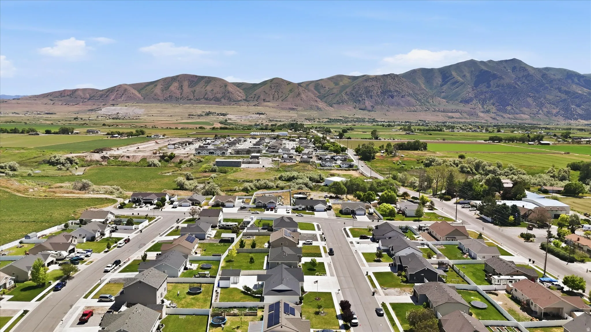 Residential neighborhood featuring paved streets and manicured lawns, set against a backdrop of distant mountains and open fields