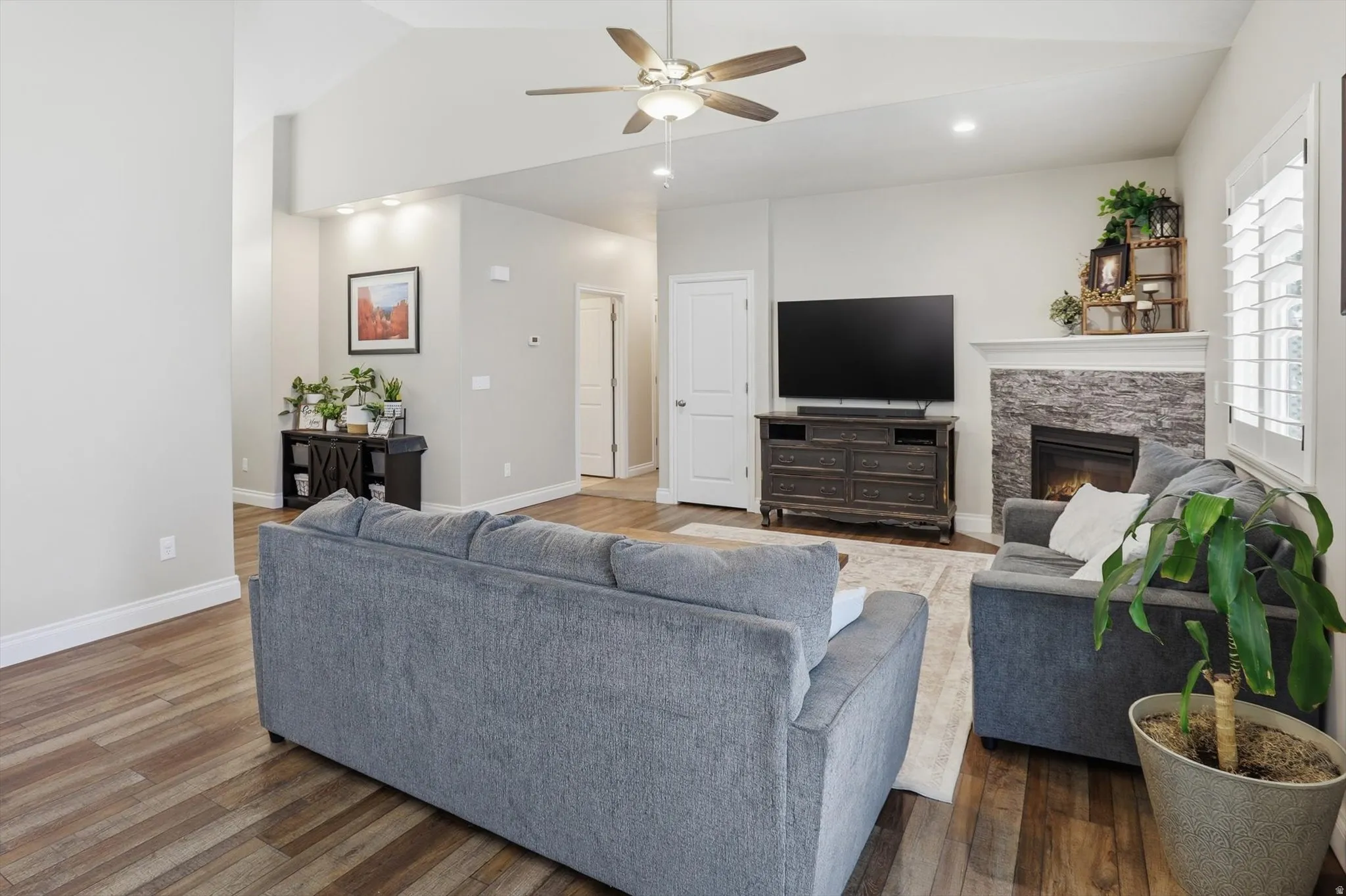 Spacious living area featuring wood-finish flooring, vaulted ceilings, and a ceiling fan with integrated lighting