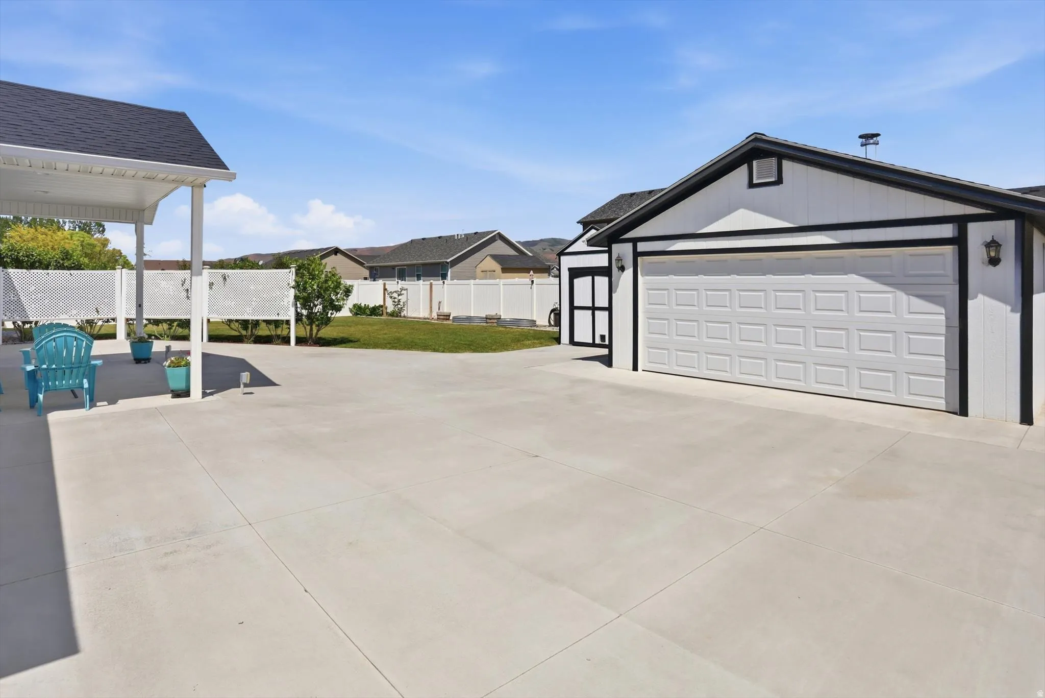 Spacious concrete driveway featuring a two-car garage with white panel doors and black trim, an additional single-car garage, an attached covered patio structure, and a manicured lawn area