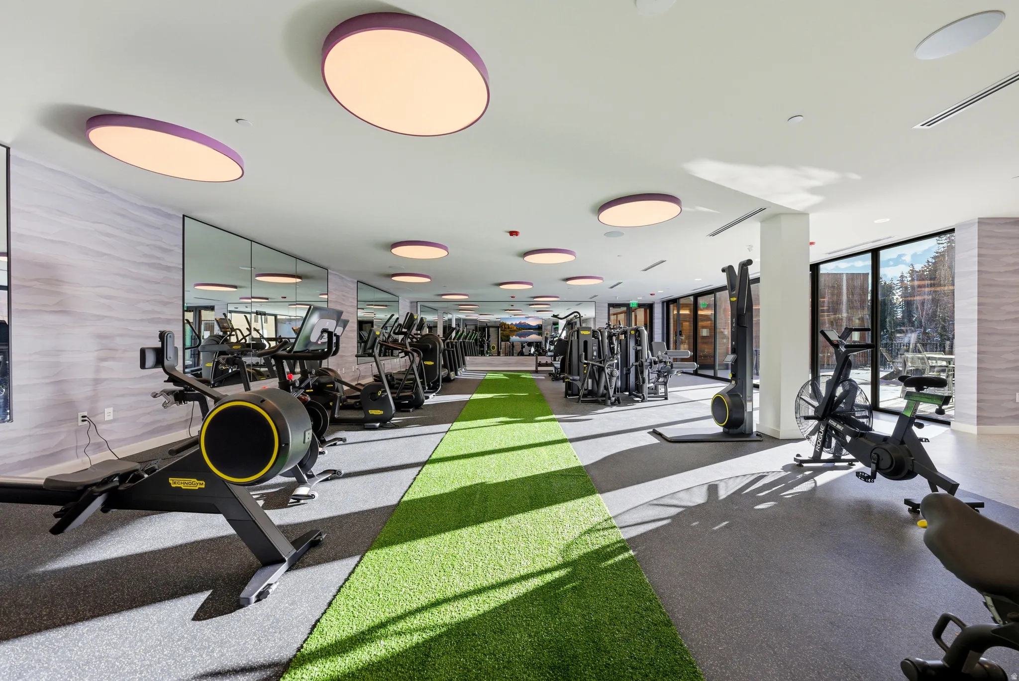 Fitness center featuring a green turf lane, rubber flooring, and floor-to-ceiling windows