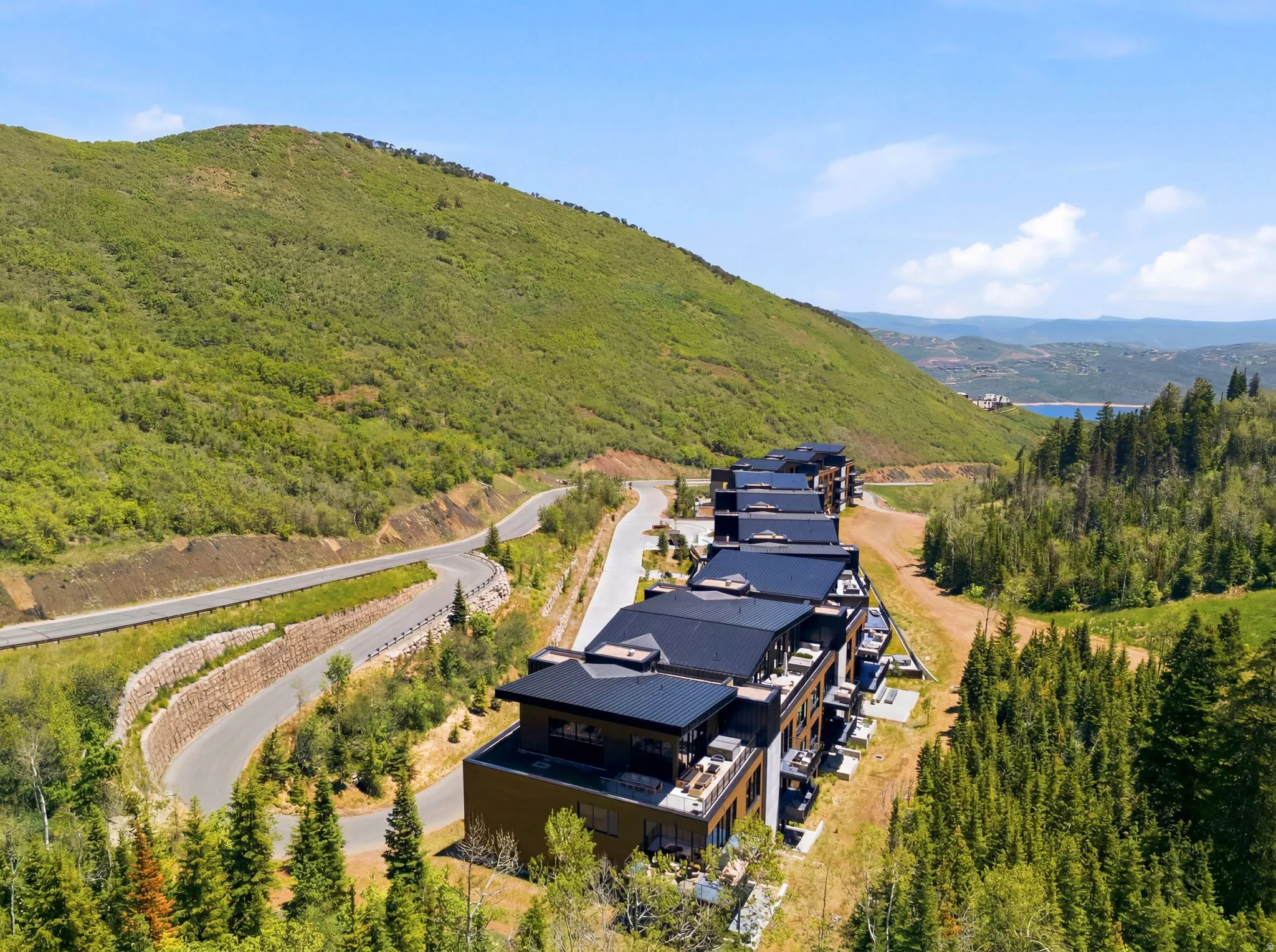 Modern multi-level structures with dark-toned roofs and private balconies, set against a verdant mountainous backdrop