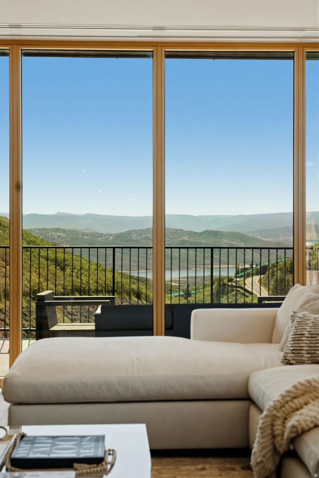 Floor-to-ceiling windows with natural wood frames offer expansive mountain and distant water scenery