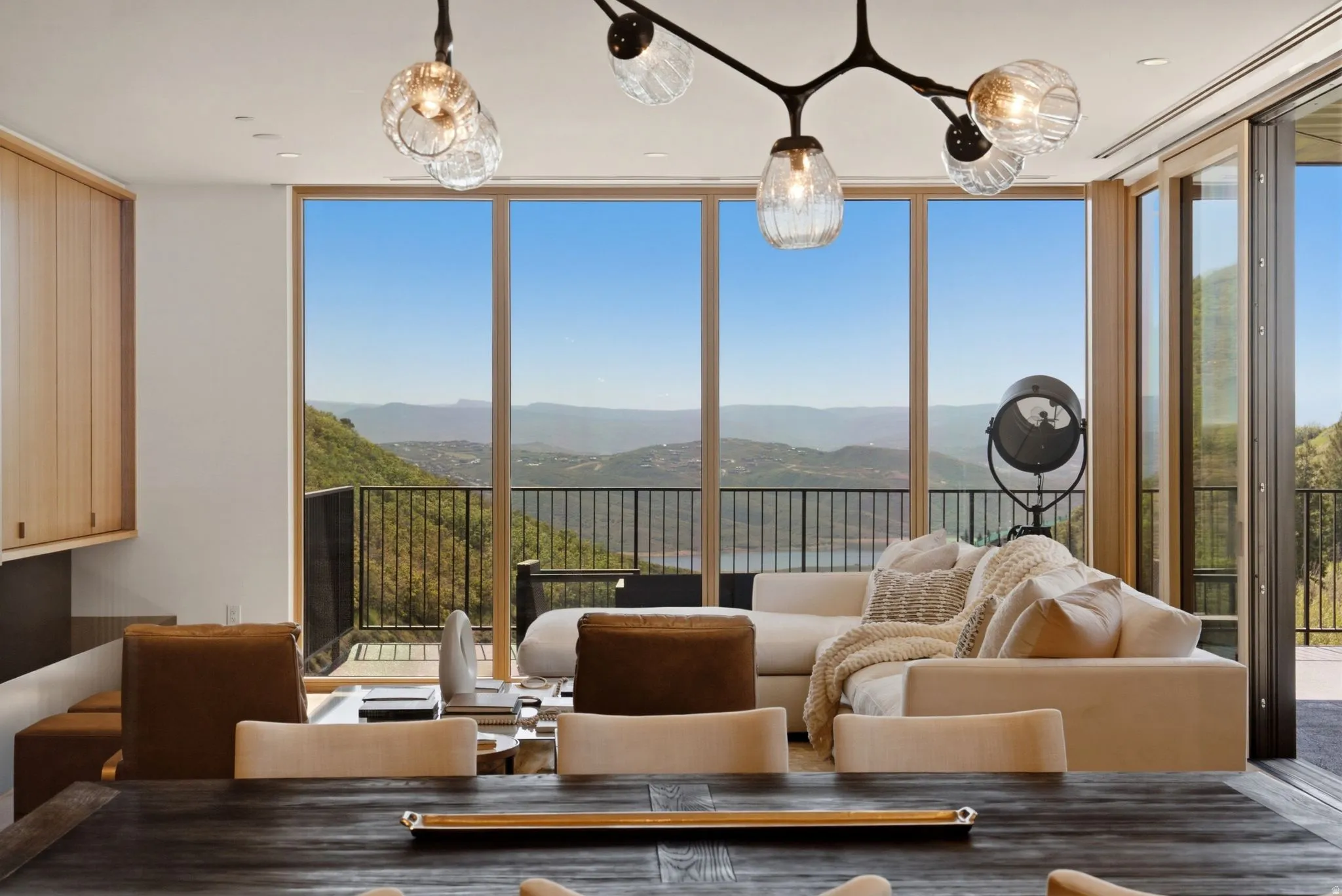 Open-concept living space with expansive floor-to-ceiling windows, showcasing a mountainous landscape with a body of water