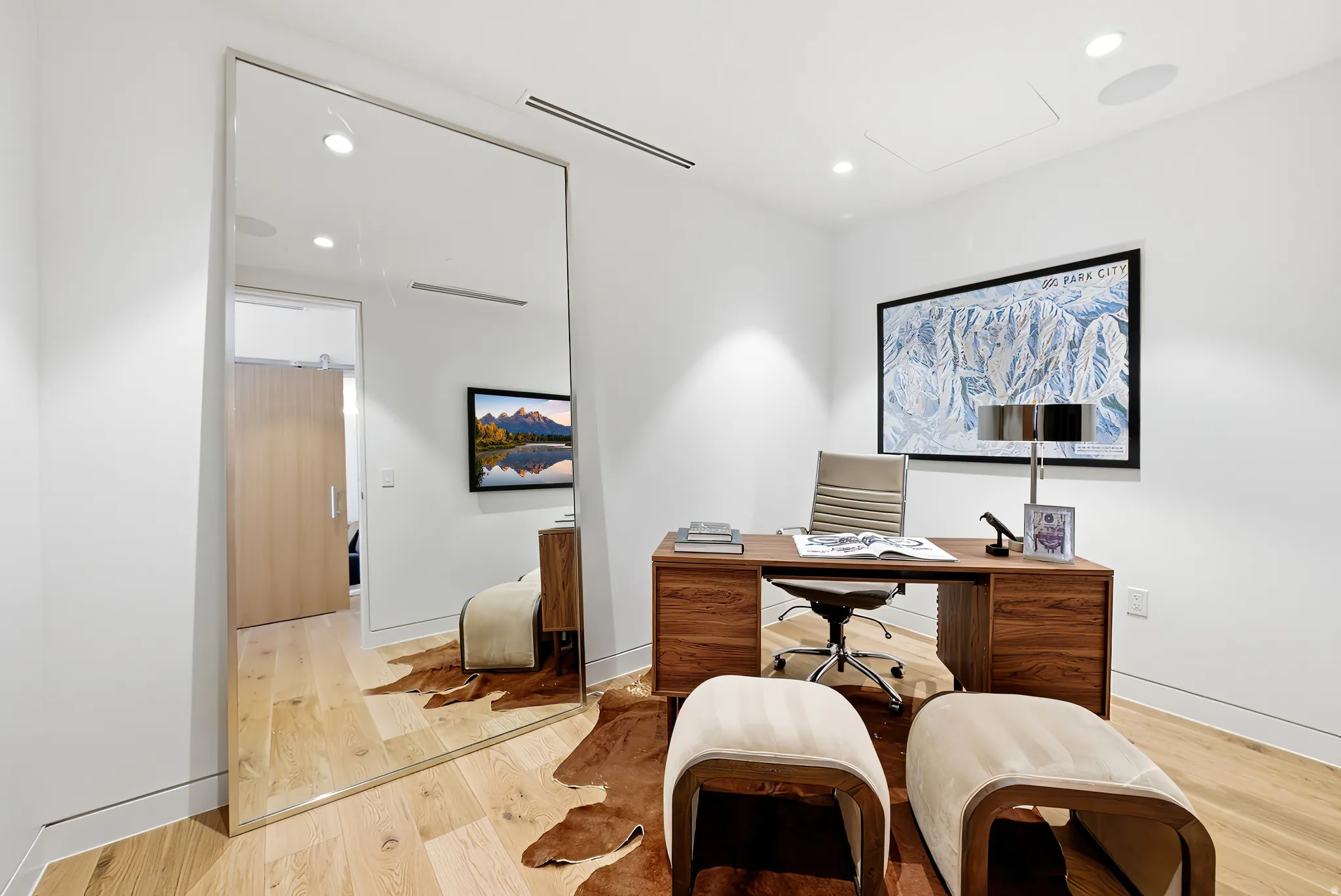 Dedicated office space featuring light wood-finish flooring, recessed ceiling lighting, and a full-length wall mirror