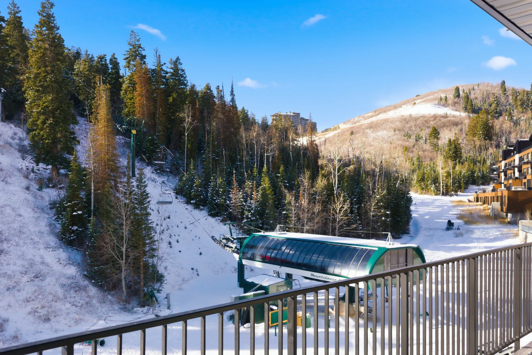 Balcony with metal railing providing alpine slope access with a ski lift, surrounded by snow-covered evergreen trees and distant mountain ranges