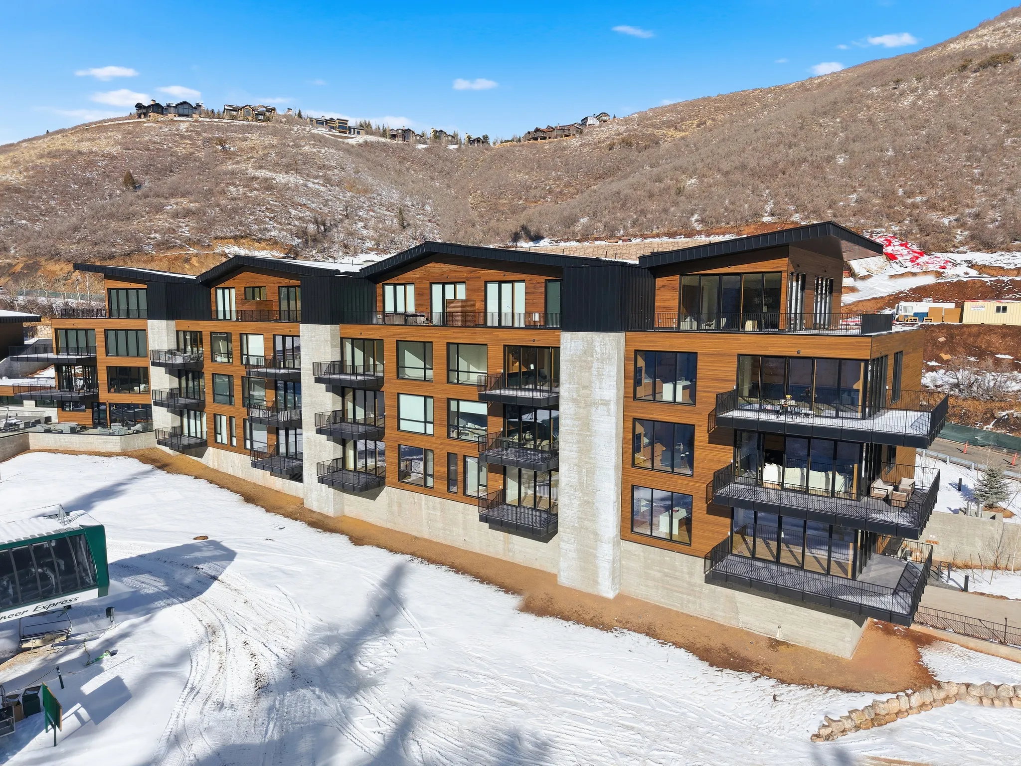Modern multi-story building featuring wood-panel siding, concrete accents, multiple balconies with glass railings, and expansive windows