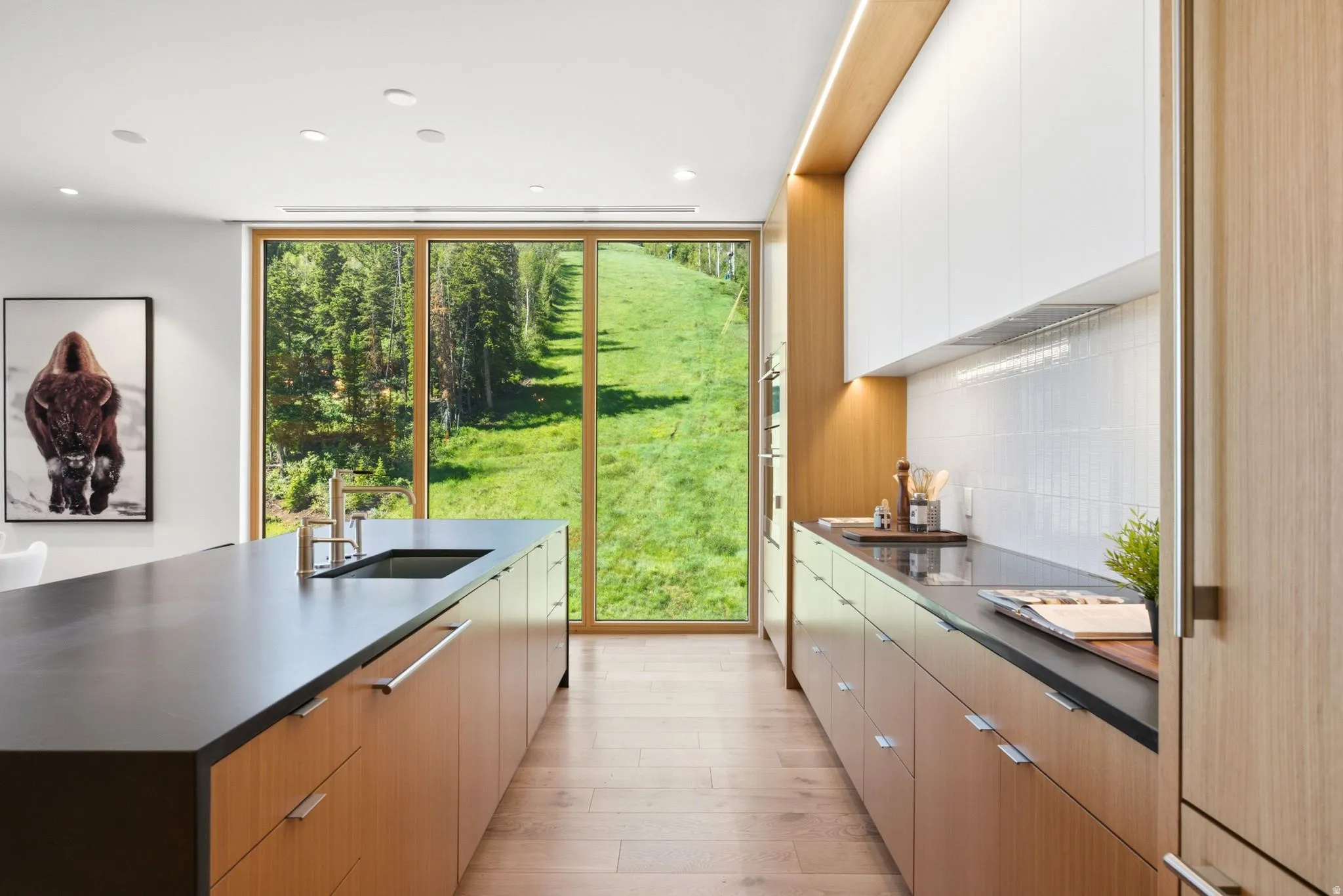 Modern kitchen featuring full-height glass paneling, wood-finish flooring, and a large center island with an undermount sink