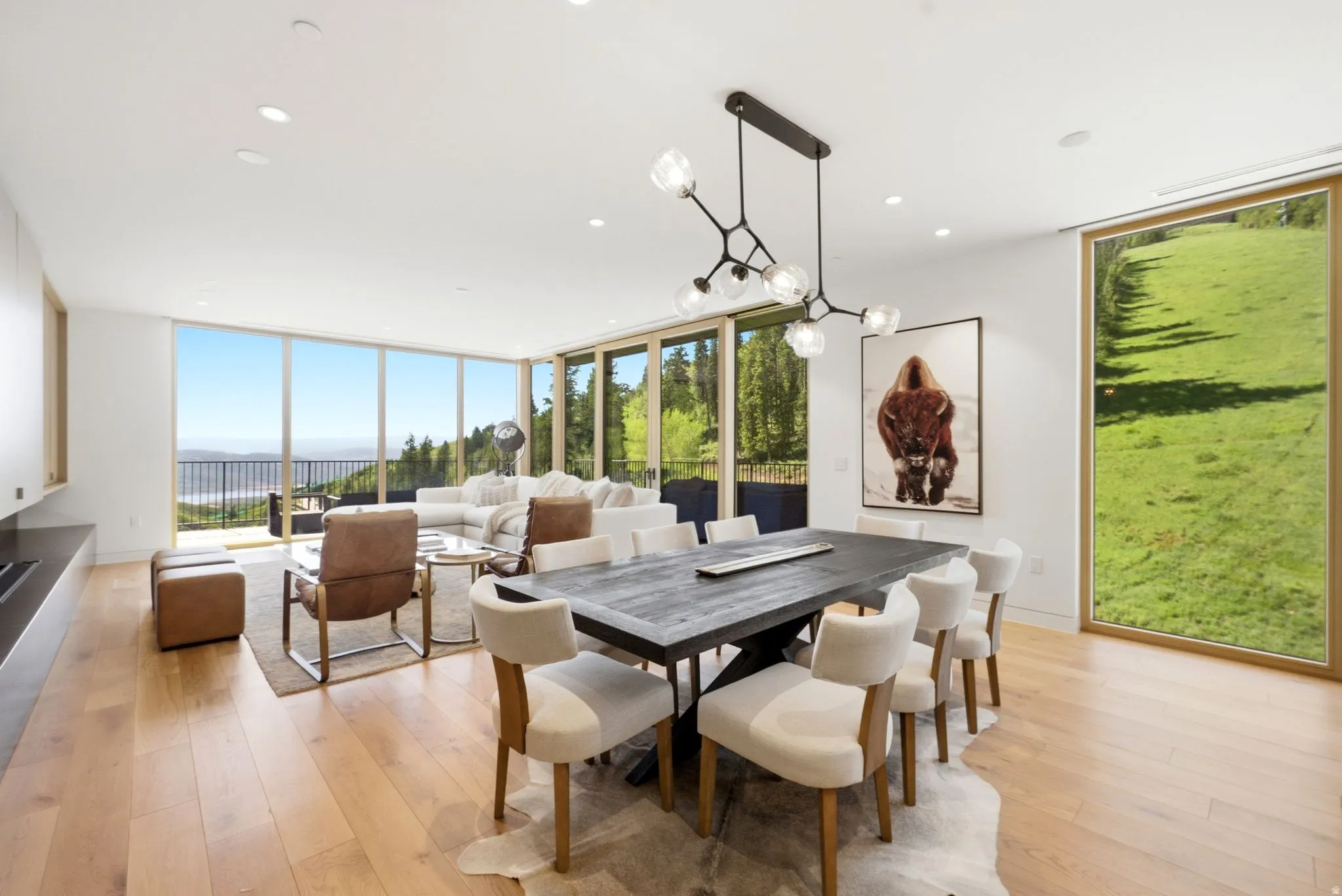 Expansive open-concept living and dining area featuring wide plank wood-finish flooring, recessed lighting, and a contemporary chandelier