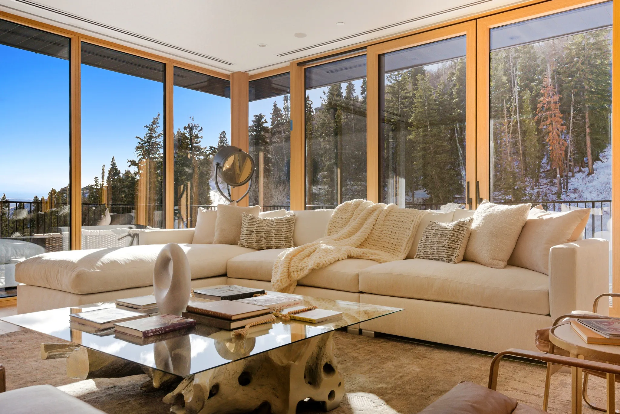 Expansive living area featuring floor-to-ceiling windows with wood frames, offering a panoramic mountain and forest backdrop