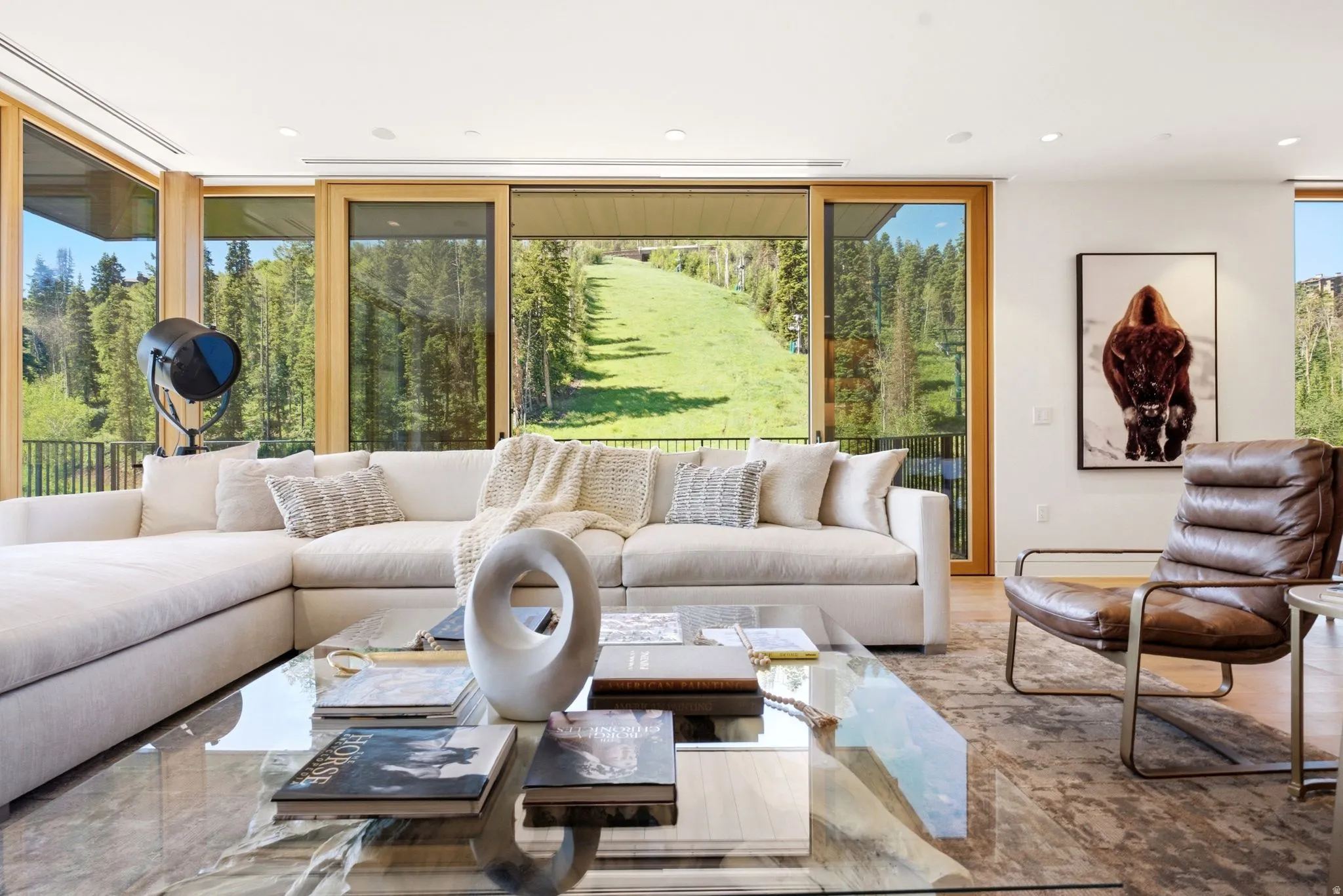 Spacious living area featuring large format windows with natural wood frames, revealing a lush green hillside