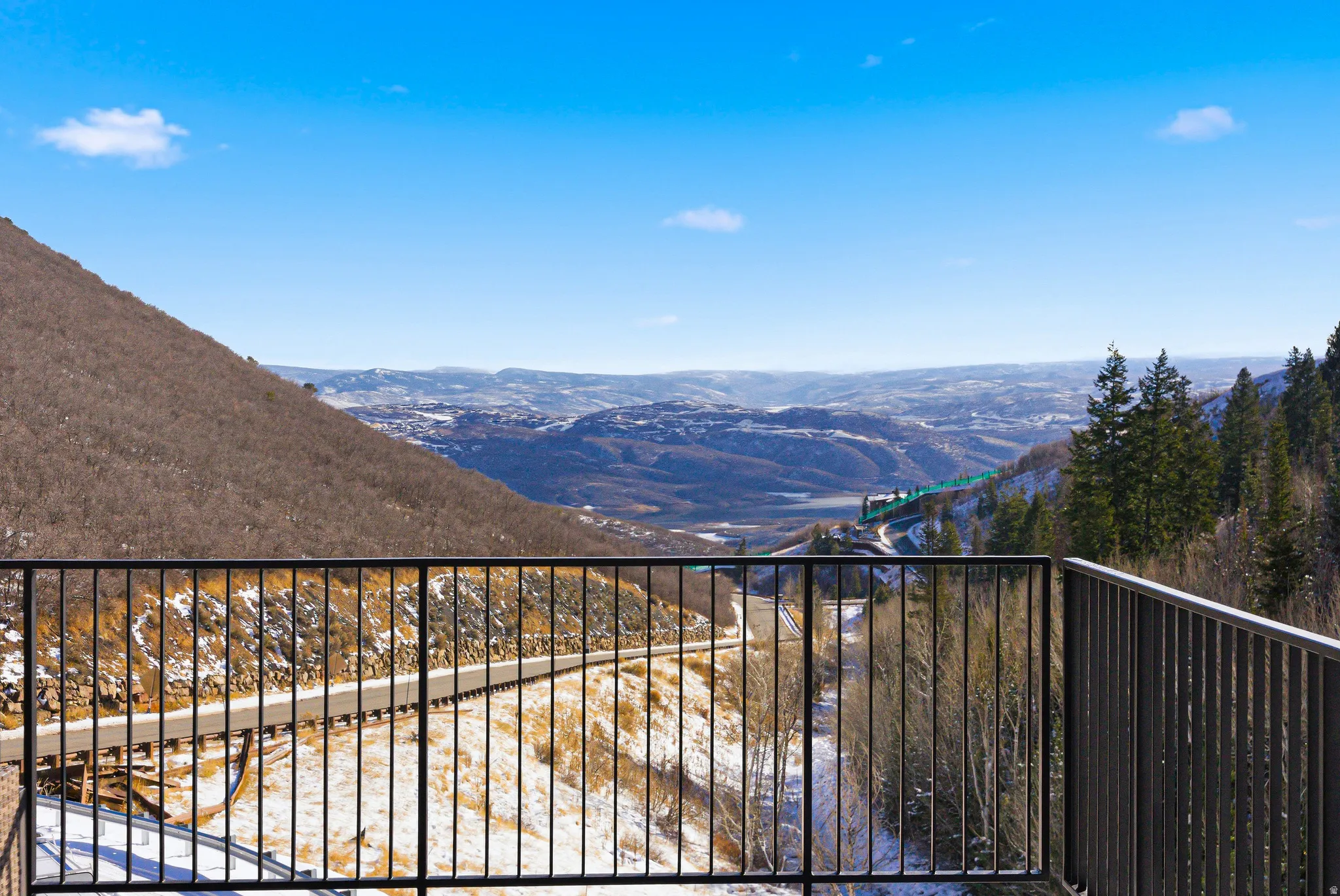 Mountain landscape featuring a distant valley, winding road, and evergreen trees