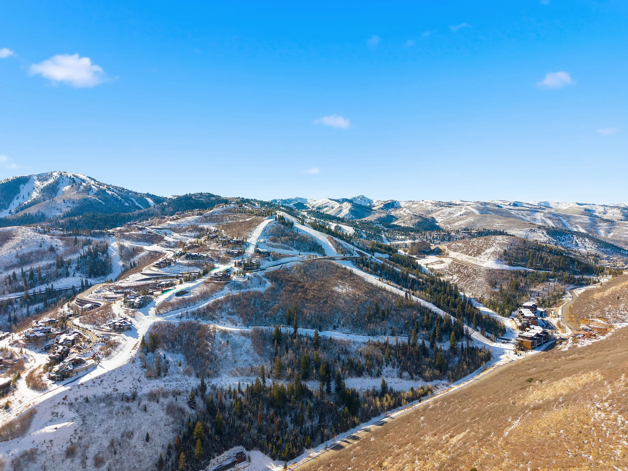 Expansive mountain landscape featuring snow-covered peaks, scattered evergreen trees, and visible ski runs