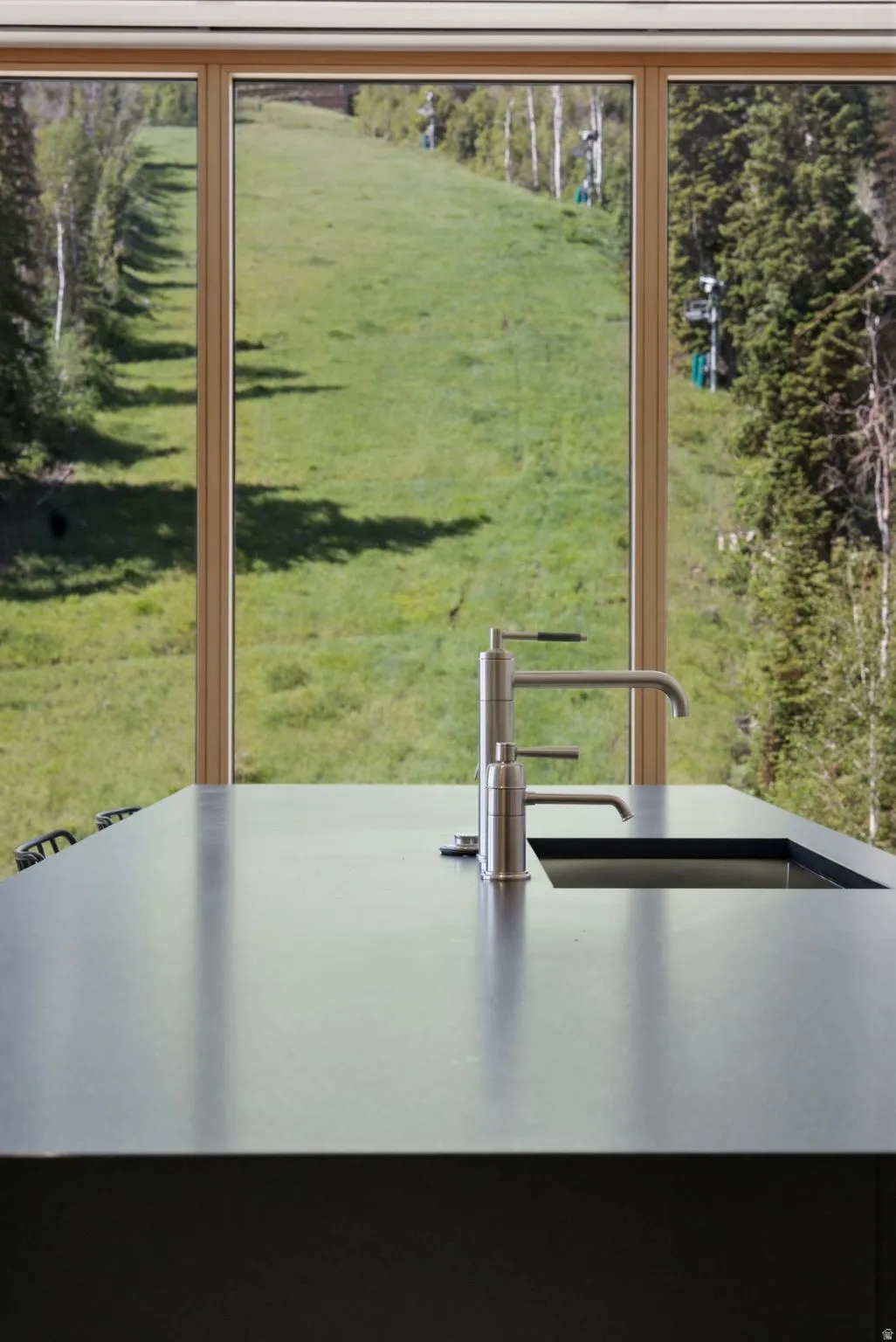 Expansive picture windows framing a vibrant green hillside and mature trees
