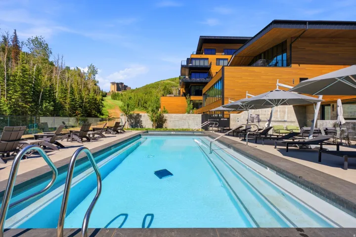 Outdoor swimming pool featuring a dark-tiled edge, metal handrails, and an adjacent concrete patio