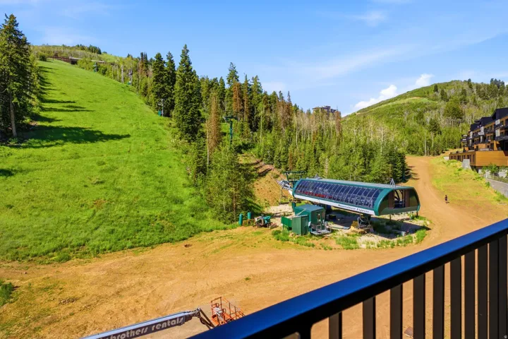 Mountain landscape featuring a ski lift structure, a vibrant green slope, and mature evergreen trees